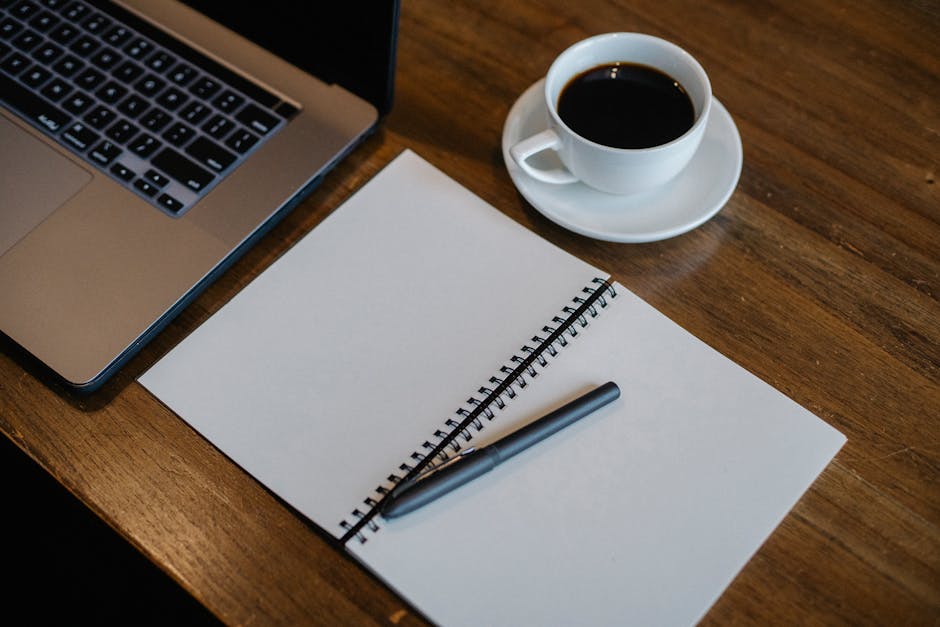 A minimalist workspace with a laptop, notepad, and coffee cup.