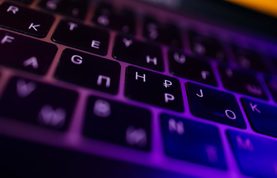 A modern computer keyboard with a blurred screen behind it.