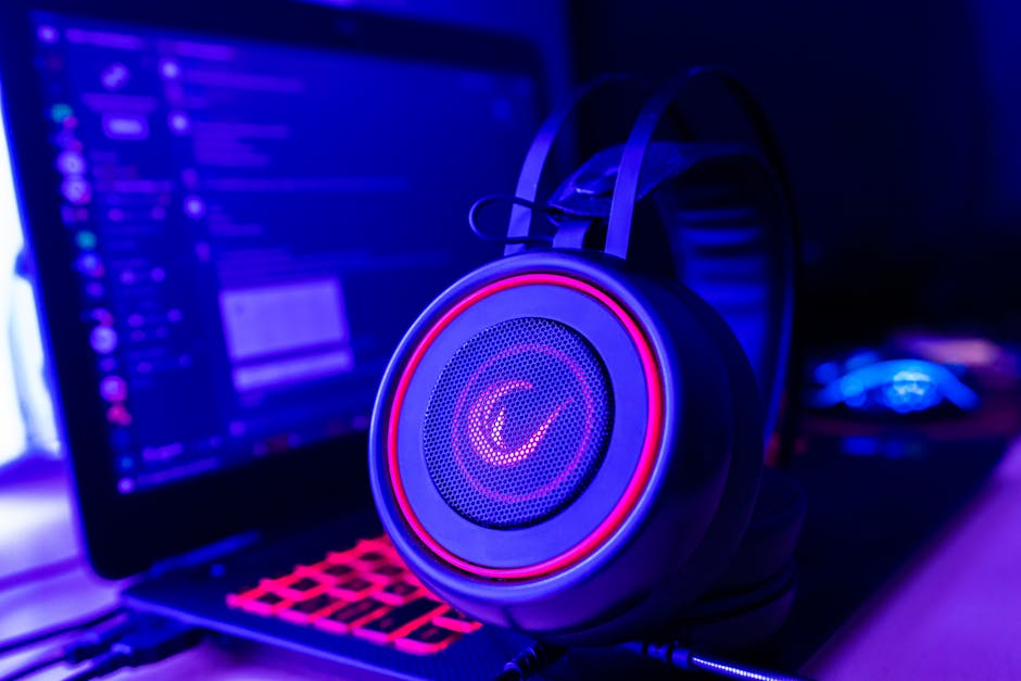 A modern workspace with a laptop, gaming headset, and colorful lighting.