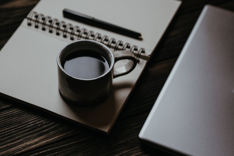 A cozy workspace with a laptop, notepad, and coffee cup on a table.