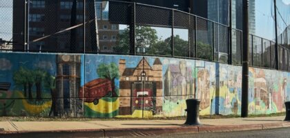 A lively urban street with colorful murals and greenery under bright sunlight.