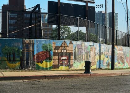 A lively urban street with colorful murals and greenery under bright sunlight.