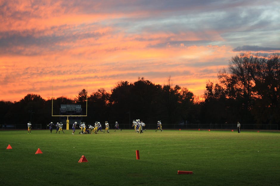 An empty football field at sunset with silhouetted goalposts.