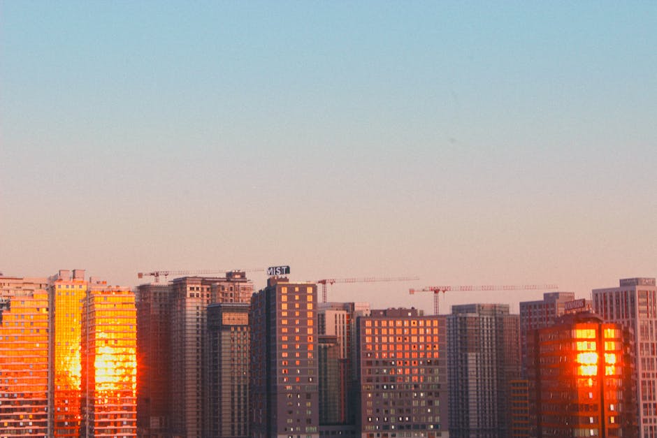 A city skyline at dusk with illuminated buildings and soft reflections.