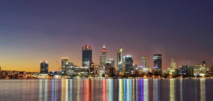 A city skyline at dusk with illuminated buildings and reflections.