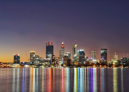 A city skyline at dusk with illuminated buildings and reflections.