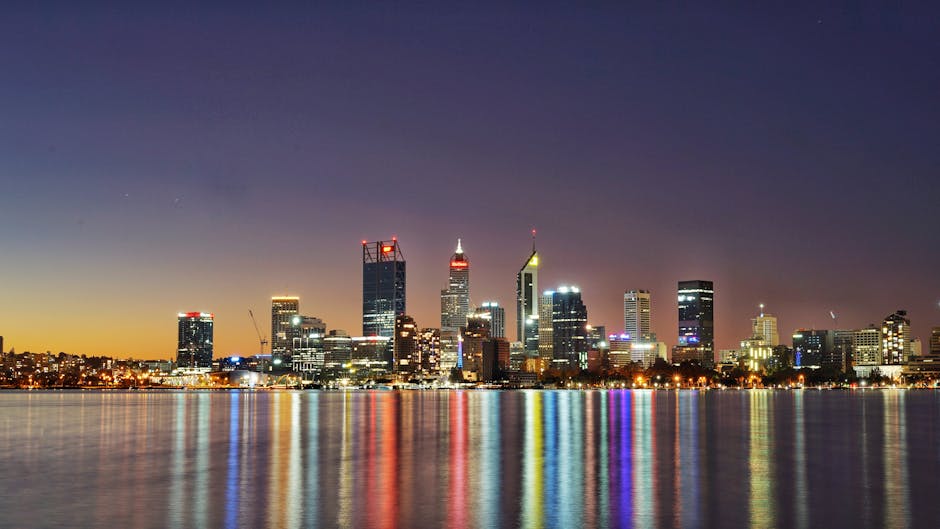 A city skyline at dusk with illuminated buildings and reflections.